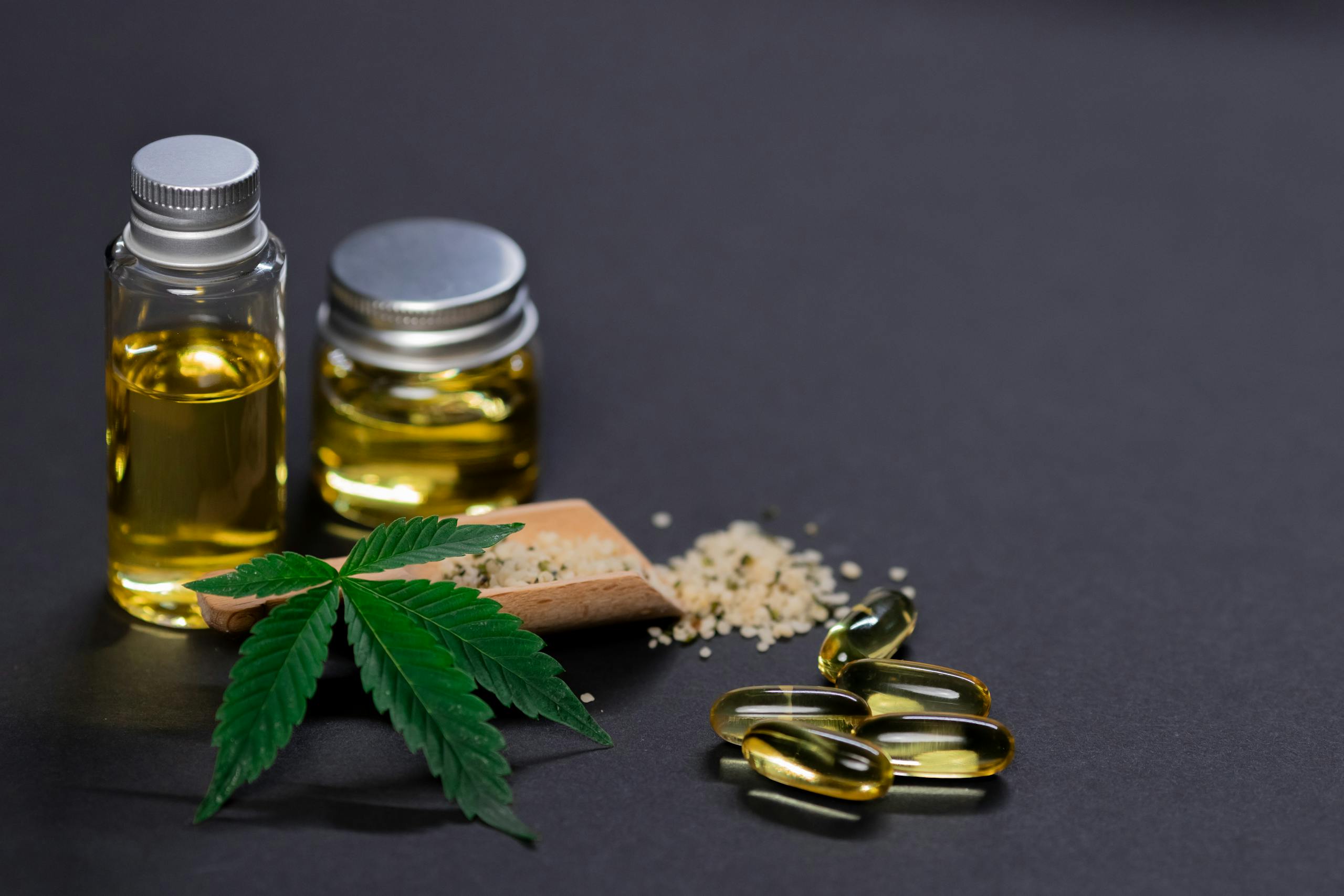 Assorted cannabis products including hemp seeds, oil, and capsules on dark background.